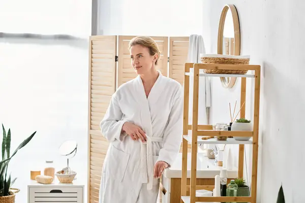 Appealing cheerful woman with blonde hair in white bathrobe posing in her bathroom and looking away — Stock Photo