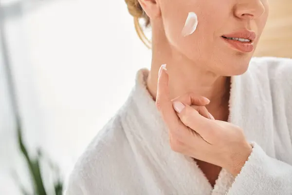 Cropped view of adult woman in comfy bathrobe applying her face cream in bathroom at her home — Stock Photo