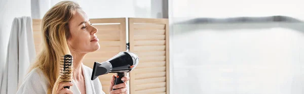 Attraente donna gioiosa in accappatoio utilizzando asciugacapelli e spazzolare i capelli lunghi a casa, banner — Foto stock