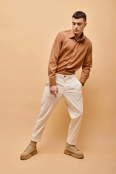 Imagen completa del joven en camisa beige, pantalones y botas posando sobre fondo beige - foto de stock