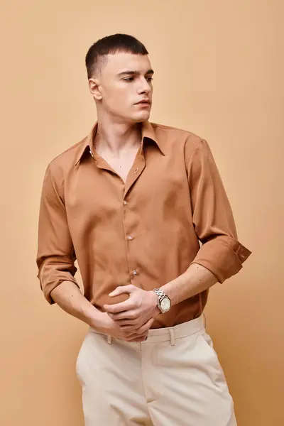 Portrait of stylish handsome man in beige shirt looking away on peachy beige background — Stock Photo