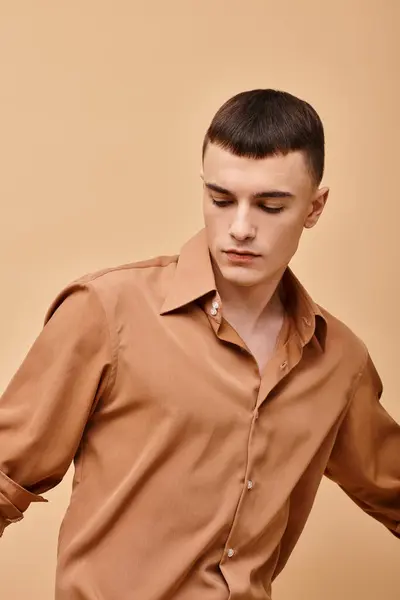 Portrait of young handsome man in beige shirt looking down on peachy beige background — Foto stock