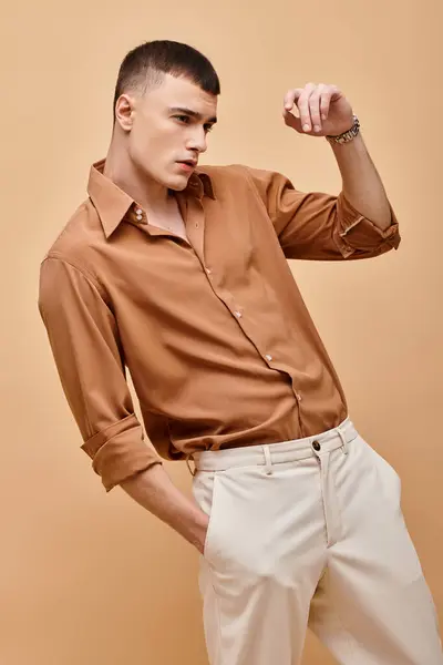 Retrato de moda de hombre guapo en camisa beige mirando hacia otro lado con la mano cerca de la cara sobre fondo beige - foto de stock