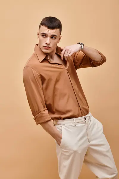 Fashion shot of stylish man in beige shirt looking away with hand on collar on beige background — Foto stock
