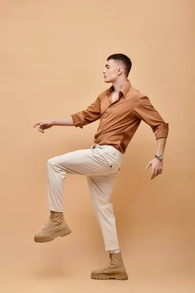 Side view photo of young man in beige shirt, pants and boots posing on beige background — Foto stock