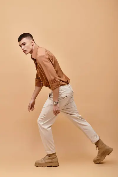 Side view image of stylish man in beige jacket, shirt, pants and boots posing on beige background — Foto stock