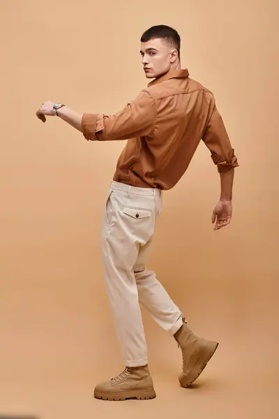 Full length photo of young man in beige shirt, pants and boots posing on beige background — Stock Photo
