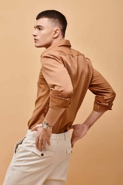 Back view portrait of stylish man in beige shirt with hand on pants on beige background — Stock Photo