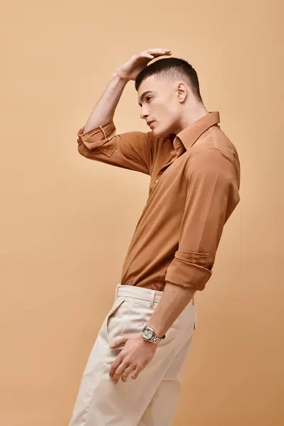 Side view photo of young man in beige stylish outfit and hand on hair posing on beige background — Stock Photo