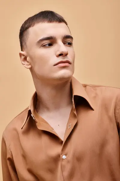Fashion portrait of stylish young man in beige shirt looking away on peachy beige background — Stock Photo