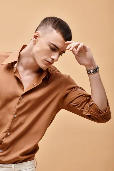 Portrait of young handsome man in beige shirt looking down on peachy beige background — Stock Photo