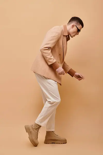 Vista lateral imagem de homem elegante em jaqueta bege, camisa, calças e botas posando no fundo bege — Fotografia de Stock