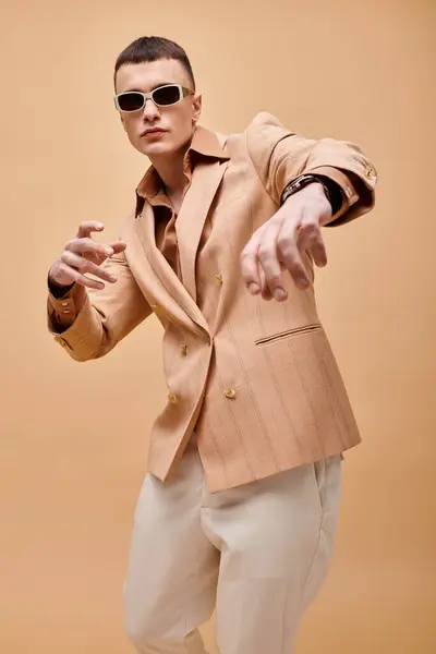 Stilvoller Mann in beiger Jacke, Hemd, Hose und Sonnenbrille posiert auf beigem Hintergrund — Stockfoto
