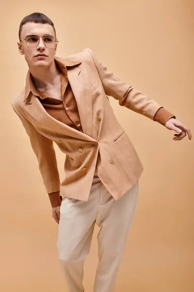 Schöner Mann in beige stylischer Jacke und trendiger Brille posiert auf pfirsichbeigem Hintergrund — Stockfoto