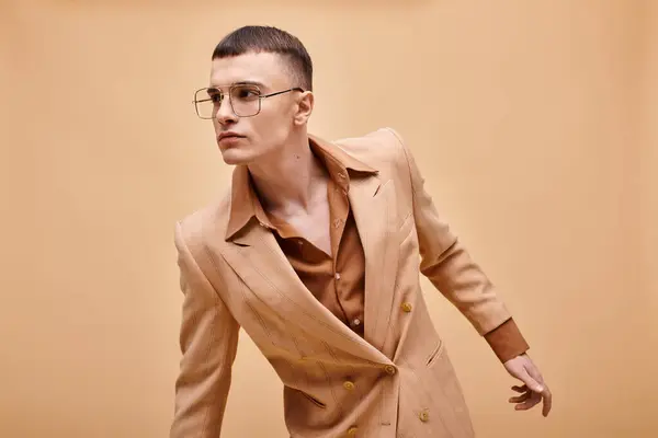 Hombre con estilo en sus años 20 posando en chaqueta beige con estilo y gafas sobre fondo beige melocotón - foto de stock