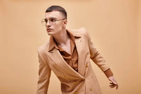 Stylish man in his 20s posing in stylish beige jacket and glasses on peachy beige background — Stock Photo