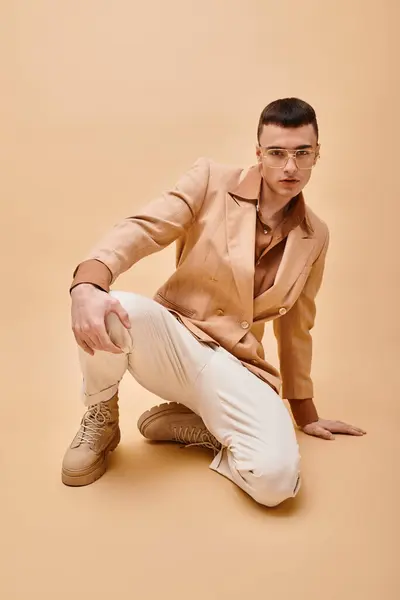 Retrato de hombre guapo en chaqueta beige y gafas sentadas sobre fondo beige melocotón - foto de stock