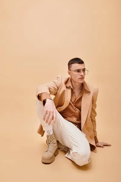 Handsome man in beige jacket and glasses sitting on peachy beige background — Foto stock