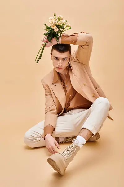 Stylish man in beige jacket sitting with flowers and glasses on beige background looking at camera — Stock Photo
