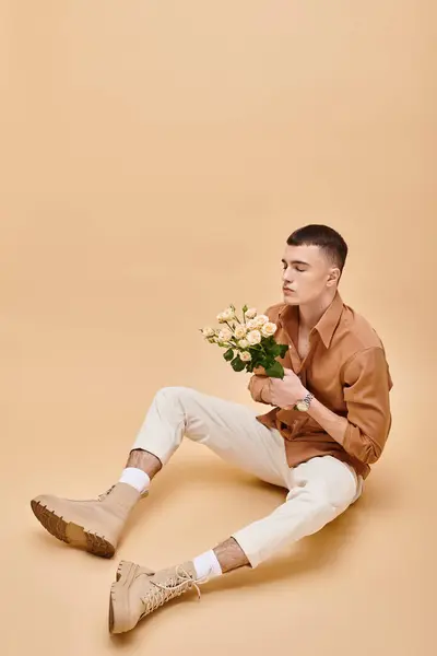 Portrait d'homme en chemise beige assis avec des fleurs roses sur fond beige yeux fermés — Photo de stock
