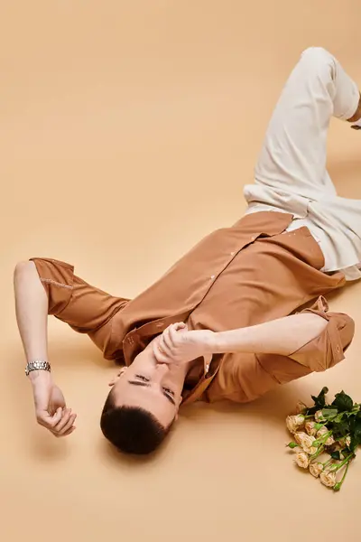 Fashion image of man in beige shirt lying with rose flowers bouquet on beige background - foto de stock