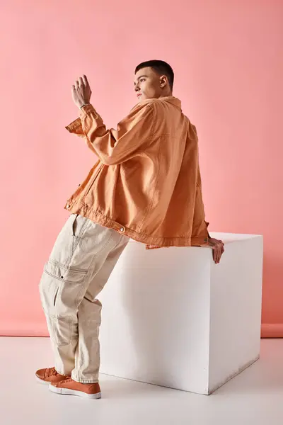 Fashion image of stylish man in beige shirt, pants and boots on white cube on pink background — Stock Photo