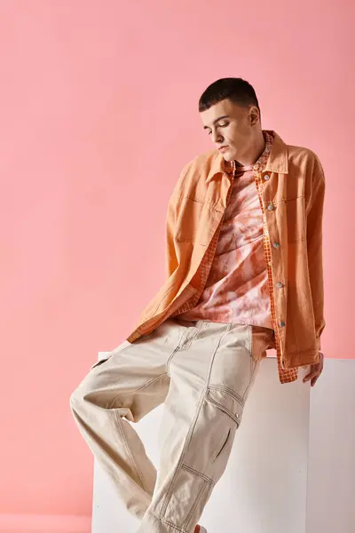 Piena lunghezza di uomo alla moda in camicia beige e pantaloni maschili alla moda su cubo bianco su sfondo rosa — Foto stock