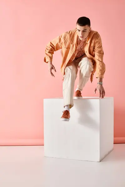 Portrait of stylish man in beige trendy outfit jumping from white cube on pink background — Stock Photo