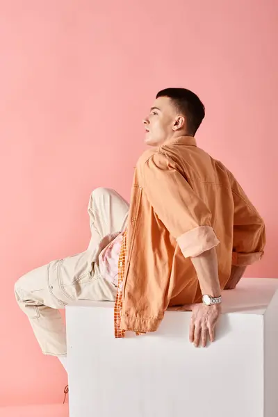 Side view image of stylish man in beige shirt, pants and boots on white cube on pink backdrop — Stock Photo