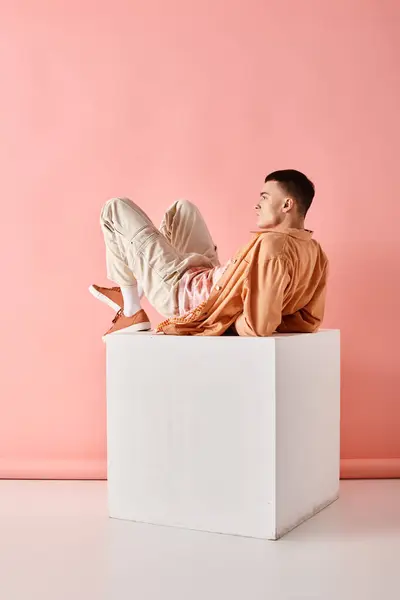 Side view photo of man in peach color outfit lying on white cube on pink background — Stock Photo