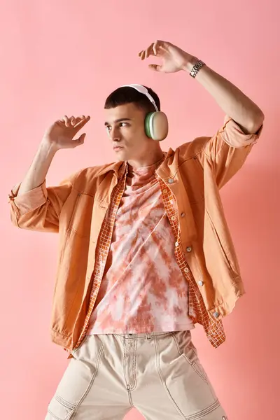 Ein Mann im mehrschichtigen Outfit mit drahtlosen Kopfhörern, der zu Musik auf rosa Hintergrund posiert — Stockfoto