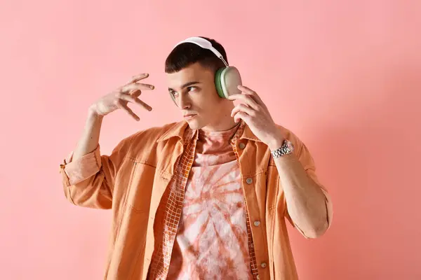 Portrait of man in layered outfit with wireless headphones dancing to music on pink backdrop — Stock Photo