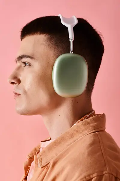 Side view of stylish man wearing wireless headphones listening to music on pink background — Stock Photo