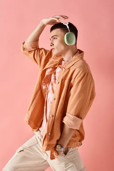 Vista lateral del hombre elegante con auriculares inalámbricos bailando con música sobre fondo rosa - foto de stock