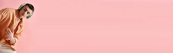 Bello uomo con cuffie wireless che ascolta musica su sfondo rosa guardando in basso, banner — Foto stock