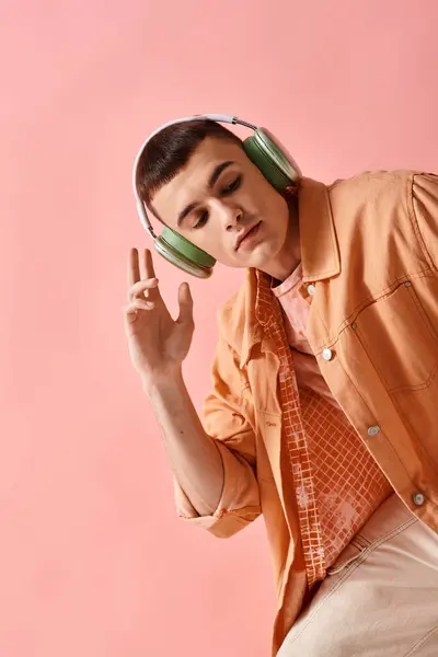 Fashionable man in layered outfit with wireless headphones listening to music on pink backdrop — Stock Photo