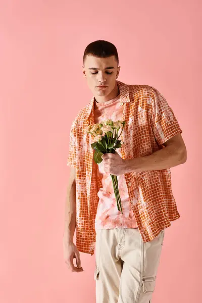 Fashion shot of fashionable man in layered outfit holding flowers on pink backdrop — Stock Photo