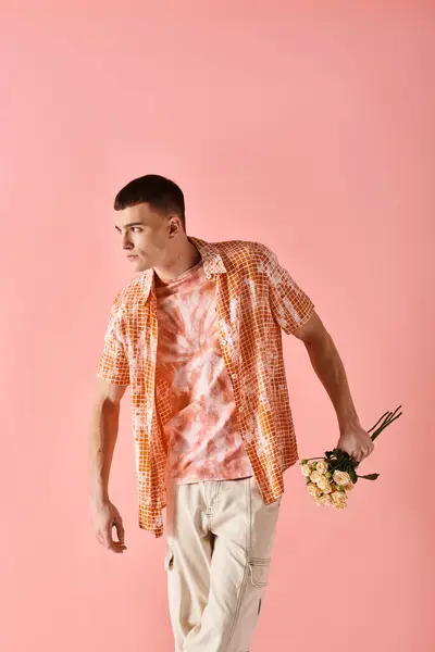 Portrait of stylish young man in layered outfit holding flowers posing on pink backdrop — Stock Photo