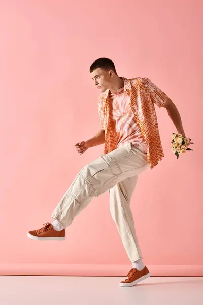 Full length image of fashionable man in layered outfit holding flowers on pink backdrop — Stock Photo