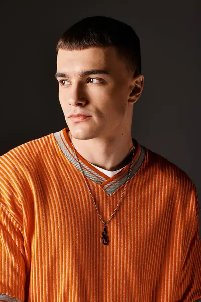 Модний портрет стильного красивого чоловіка в помаранчевому джемпері, який дивиться на сірий фон — стокове фото