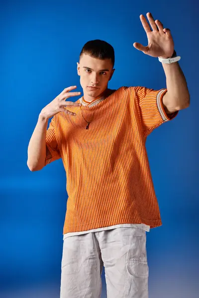 Fashionable man in his 20s in trendy orange shirt and white shorts posing on deep blue background — Stock Photo