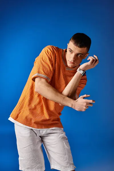 Fashion shot of stylish man in orange shirt and white shorts moving on blue background — Stock Photo