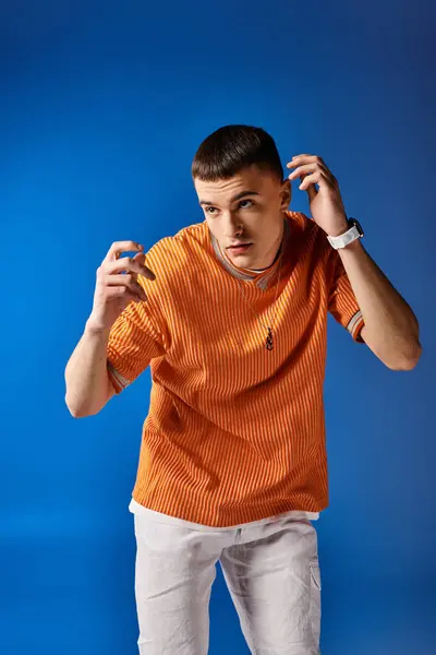 Modeporträt eines gutaussehenden Mannes in orangefarbenem Hemd und weißen Shorts, der auf blauem Hintergrund posiert — Stockfoto