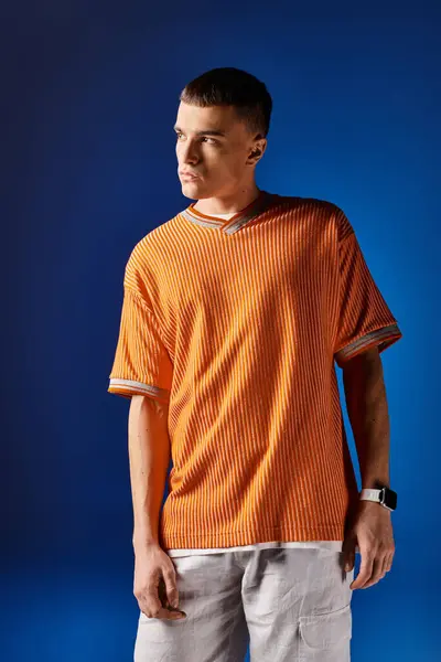 Fashionable man in his 20s in orange shirt and white shorts posing on dark blue background — Stock Photo