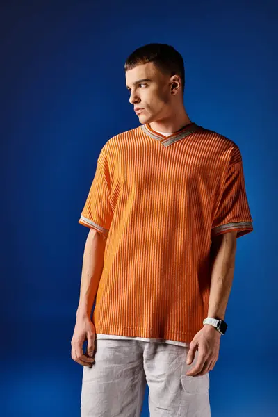 Retrato de moda de hombre guapo en camisa naranja y pantalones cortos blancos posando sobre fondo azul - foto de stock