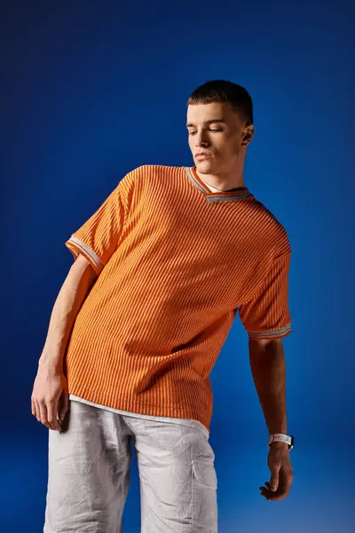 Fashionable man in his 20s in orange shirt and white shorts posing on dark blue background — Stock Photo