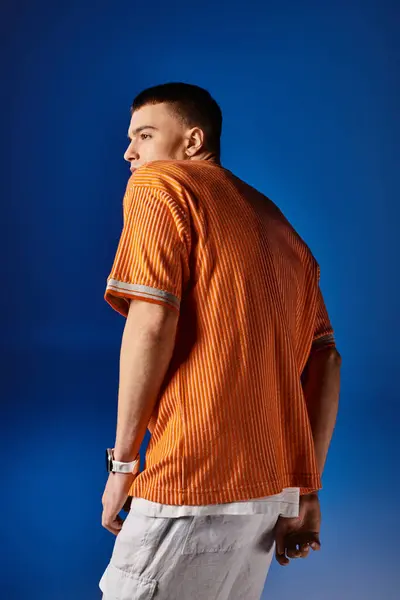 Side view shot of handsome man in orange shirt and white shorts posing on blue backdrop — Stock Photo