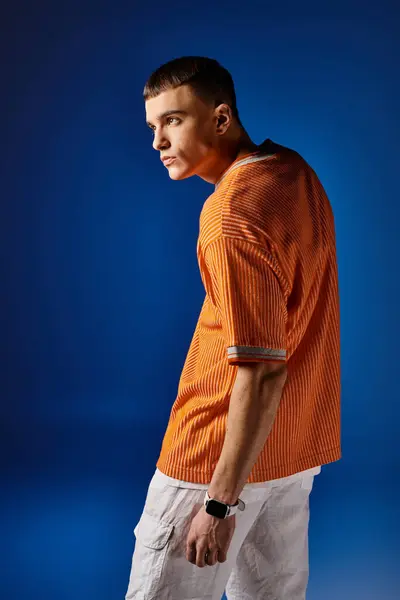 Side view portrait of stylish man in orange shirt and white shorts posing on blue backdrop — Stock Photo