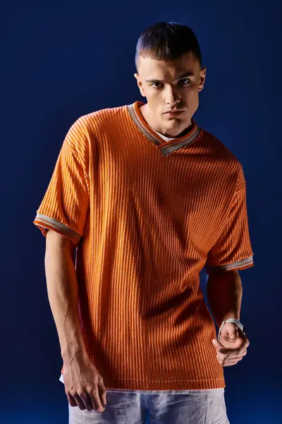 Retrato de moda de hombre guapo en camisa naranja y pantalones cortos blancos posando sobre fondo azul oscuro - foto de stock