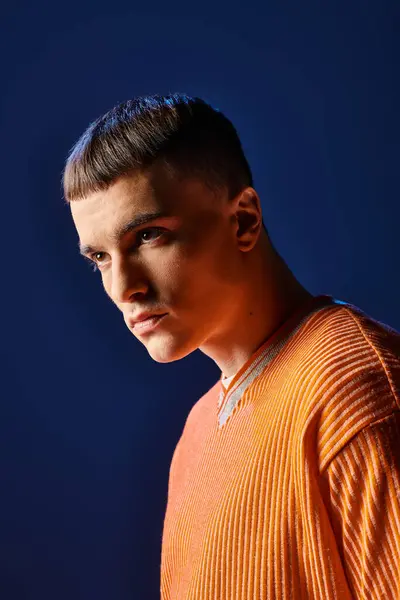 Retrato de un hombre joven y elegante con camisa naranja mirando hacia otro lado sobre fondo azul oscuro - foto de stock